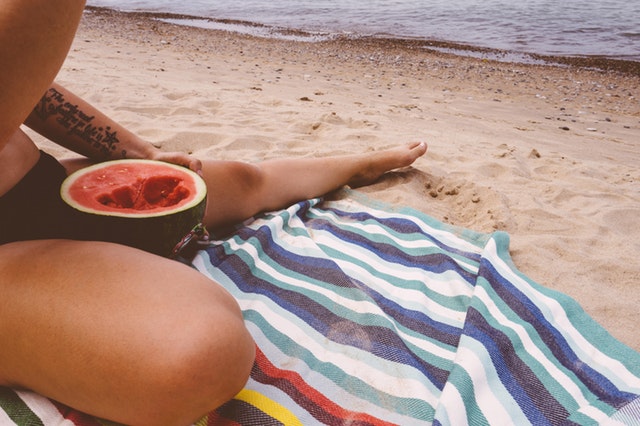Žena v plavkách sedí na pláži a konzumuje melón