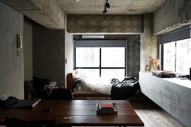 Moderná spálňa s betónovými stenami, posteľou, kreslom a stolom.jpg